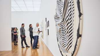 Group of visitors in the exhibition room of the Art Museum, in the foreground a large, round work of art