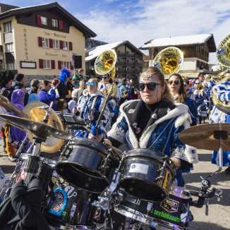 Guggenmusik in colorful costumes plays at the 2024 carnival parade in snowy Malbun in Liechtenstein.