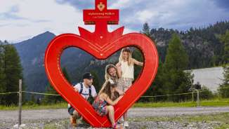 Family poses at the red heart frame along the Alpherzweg in Malbun, Liechtenstein, surrounded by alpine nature and mountains.