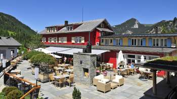 Exterior view of the restaurant in the sunshine, with red façade and mountainous panorama.