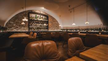 Atmospheric interior of the WY Weinbar with illuminated bar shelves, natural stone wall and elegant furnishings in the vaulted cellar.