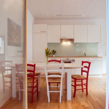Bright living and dining area with modern kitchenette and red and white chairs in the guest house at Camping Mittagsspitze.