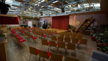 Large, light-flooded event room at the Kreativ Akademie with stage, red curtains and rows of chairs - ideal for seminars, lectures and creative events in Liechtenstein.