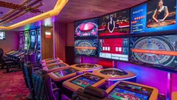 Modern gaming tables with digital screens and several roulette and card game options in the atmospherically lit Casino Schaanwald.