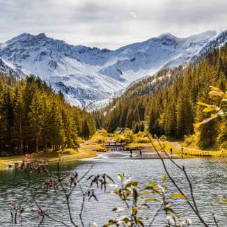 Autumn atmosphere in Steg, Liechtenstein, with colorful forests, a clear lake and snow-covered Alps in the background