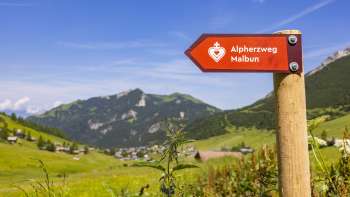 Alpine Heart Trail signpost with the mountain village of Malbun in the background