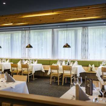 An inviting dining area with round tables and soft green chairs, furnished in a modern, natural style.