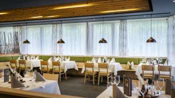 An inviting dining area with round tables and soft green chairs, furnished in a modern, natural style.