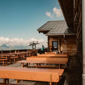 Empty wooden benches on the panoramic terrace of the Sareis hut with a view of the Alps - ideal for a break during a hike or ride on the mountain railroad.