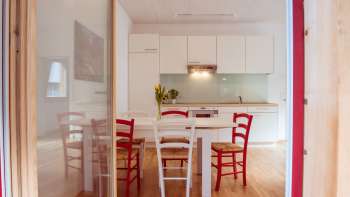 Bright living and dining area with modern kitchenette and red and white chairs in the guest house at Camping Mittagsspitze.