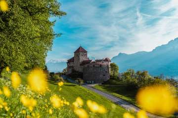 Vaduz Castle surrounded by blossoming spring meadows and mountains in the background - Liechtenstein's landmark in all its glory