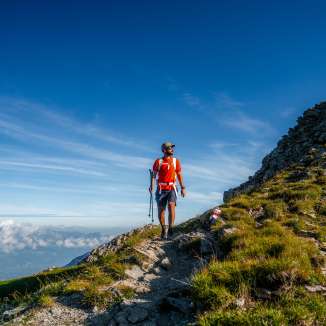 Hiker with a red shirt on the ridge of the Drei Schwestern mountain chain along Route 66 with a view over the Alpine landscape in Liechtenstein
