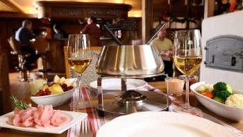 Close-up of cheese fondue set with fresh bread, vegetables and wine in a stylish setting