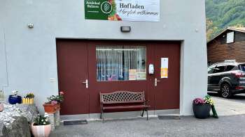 Entrance to the Aeulehof farm store with red gate, bench and floral decorations in Triesen, Liechtenstein.