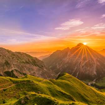 Sunset behind the mountain peaks near Malbun in Liechtenstein with alpine pastures, mountain paths and golden light