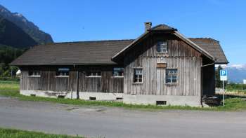 Historic wooden building of the old sawmill in Schaanwald against an alpine backdrop under a blue sky.