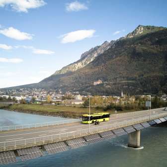 Yellow LIEmobil bus crosses the Rhine bridge near Vaduz with a mountain panorama in the background - Experience Liechtenstein