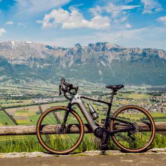 Gravel bike leaning against the fence above Planken with panoramic views over the Rhine Valley and the Alps in Liechtenstein - perfect spot for cyclists