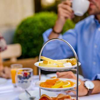 Breakfast with sausage, cheese and fresh fruit on an etagere in Vaduz while a guest drinks coffee
