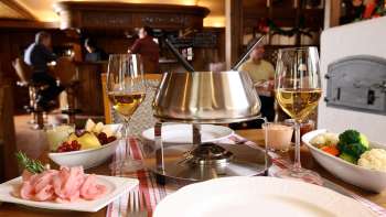 Close-up of cheese fondue set with fresh bread, vegetables and wine in a stylish setting