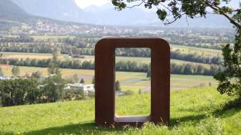 Sculpture "Resonare" made of rusty metal on the Krest hill with a view of the Rhine Valley and the mountains in the background.