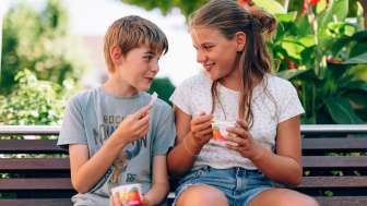 Enjoying ice cream in Liechtenstein - summer fun for children Two children sit on a park bench in Liechtenstein and eat ice cream - smiling faces, flowers and a summer atmosphere in the countryside
