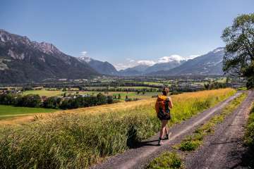 Woman hiking on a dirt road with a panoramic view over the Rhine Valley in Liechtenstein