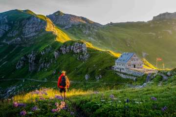 Hiker looks at the Pfälzer hut in Liechtenstein, surrounded by a green mountain landscape and Alpine panorama in the evening light