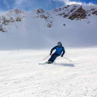 Skiers on a wide ski slope in Malbun, Liechtenstein, surrounded by snow-covered Alpine slopes and a bright blue sky
