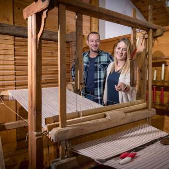 A couple looks at a functioning historical loom in the Walser Museum Triesenberg in Liechtenstein, surrounded by wood paneling