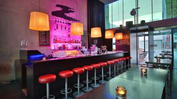 Modern bar with long counters, red bar stools and stylish lighting in pink and orange