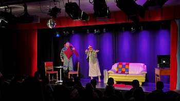 Cabaret scene at K-BUM in Liechtenstein - colorful stage with sofa, actor duo and audience in the hall.