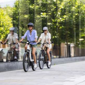 Two women on e-bikes ride through the modern center of Vaduz in Liechtenstein, with its glass façade and urban flair