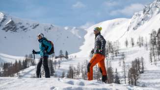 Two people winter hiking through the snow-covered landscape of Malbun with snow-capped mountains in the background