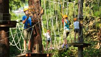 Children and adolescents with helmets in the high ropes course of the Triesen rope park in Liechtenstein, secured on climbing elements in the forest