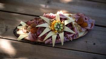 An artfully arranged wooden board with different types of sausage, cheese and decoration of edible flowers, served on a wooden table. An artfully arranged wooden board with different types of sausage, cheese and decoration of edible flowers, served on a wooden table.