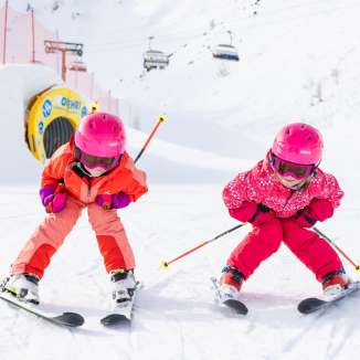 Two children with pink helmets are skiing on the slopes in Malbun in the sunny winter weather, laughing.