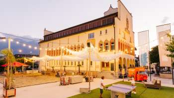 Vaduz Town Hall Square in the evening during a busy market day with crowds of people, stalls and atmospheric lighting.