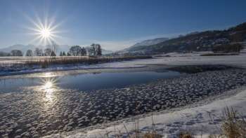 Sunrise at Lake Egelsee in Mauren in winter with glistening ice, snow and a sunny mountain backdrop.