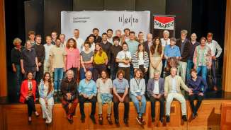 Group photo of the participants and instructors of the Liechtenstein Guitar Days (LiGiTa) on a stage in front of a banner with the event logo