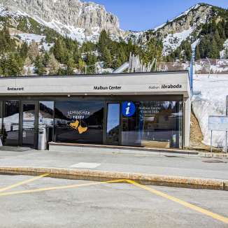 Entrance to the Malbun Center with tourist information and restaurant in front of a snow-covered mountain landscape in Malbun, Liechtenstein