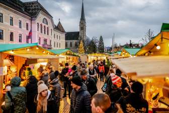 Atmospheric evening shot of the Christmas market in Vaduz 2018 with festively decorated market stalls and crowds in front of the government building and cathedral