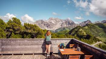 Hiker gazing at an impressive Alpine panorama from the wooden terrace by the viewing platform.