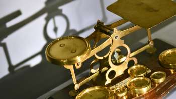 Picture of an antique gold-colored beam scale with various weights, exhibited in the PostMuseum in Vaduz.
