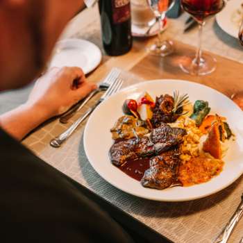 Close-up of a main course with meat, vegetables and fine sauces, accompanied by red wine