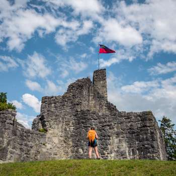 Hiker stands in front of the imposing ruins of Schellenberg Castle under a blue sky with a flag.