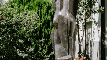 Modern bronze figure sculpture, standing between flowers and bushes in Vaduz - work by Herbert Albrecht.