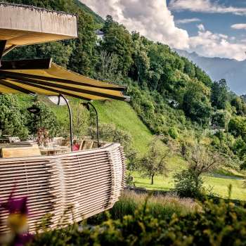 Sunny terrace with blooming flowers and elegantly laid tables with a view of the valley