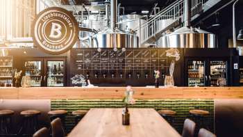 Cozy taproom in the Liechtensteiner Brauhaus with wooden tables, tapping system and view of the brewing kettles