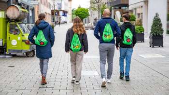 Four young people with green FoodTrail backpacks stroll through the town of Vaduz